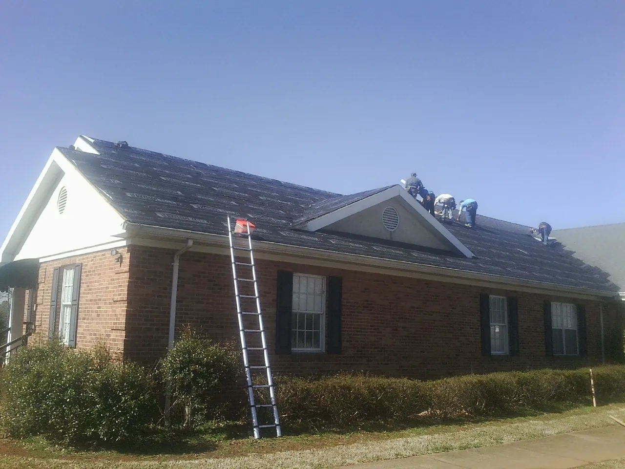 Crew tearing shingles off a brick ranch roof with a ladder set — Emergency Roof Repair work by our crew in Phillipsburg