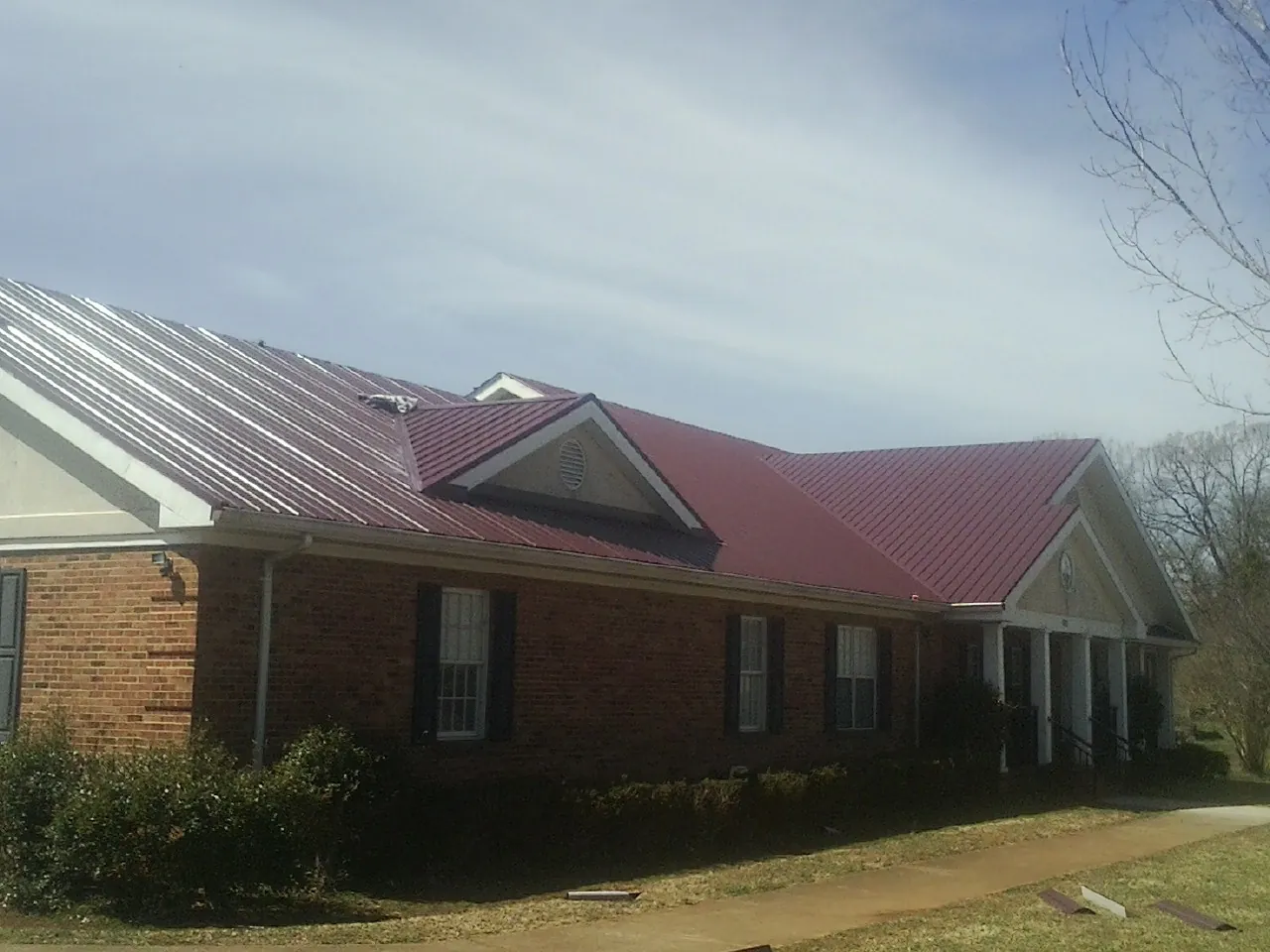 Red metal roof with gabled entries on a long brick building, from a Hail Damage Roof Repair job in Phillipsburg
