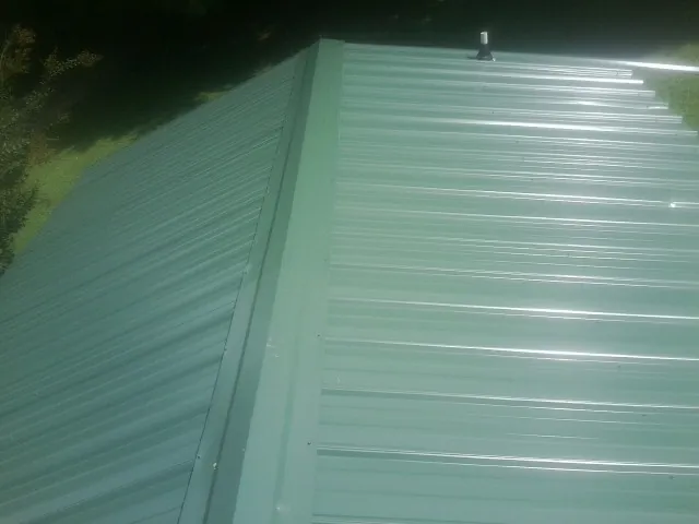 New green metal panels meeting at the ridge of a roof — Flat Roof Repair work by our crew in Phillipsburg