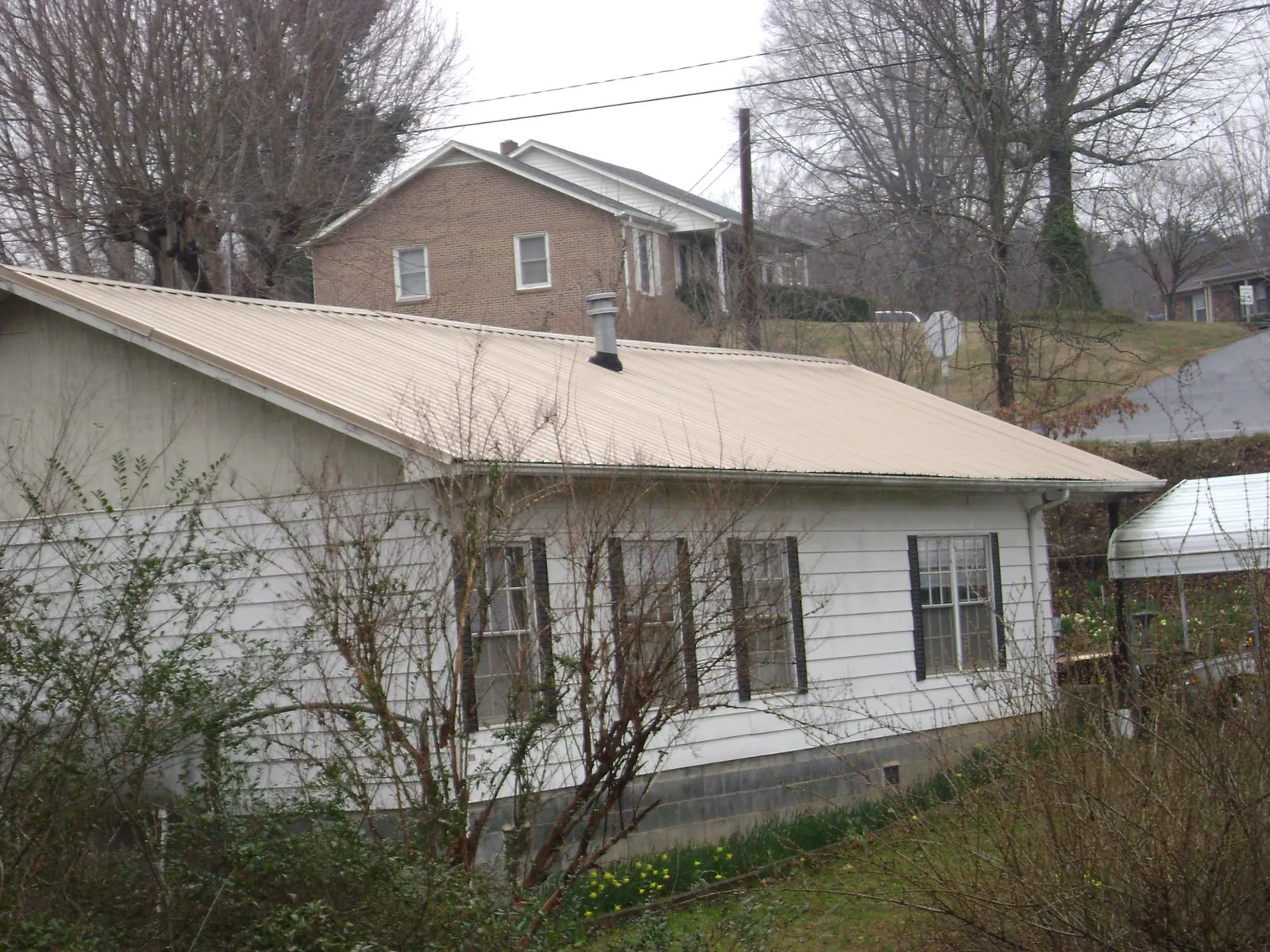 Tan metal roof on a white sided house set into a hillside — Commercial Roofing by Roofing Brothers in Phillipsburg