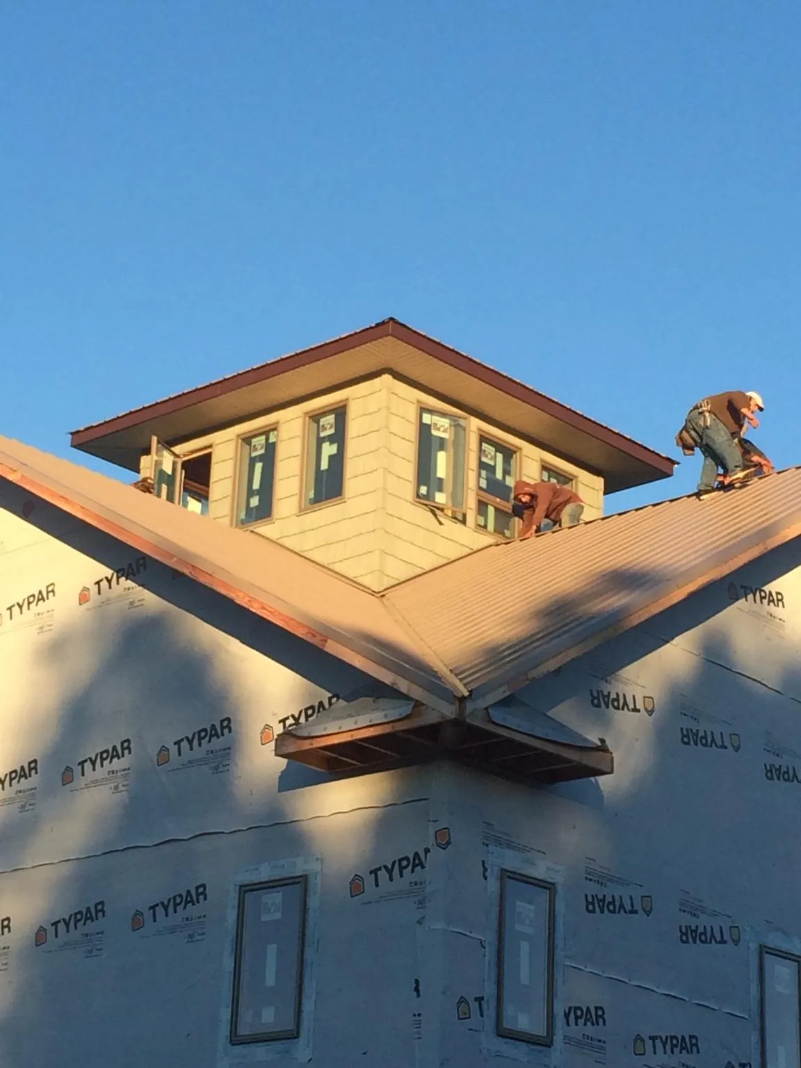 Roofers working around a rooftop cupola on a new metal roof at sunset in Phillipsburg